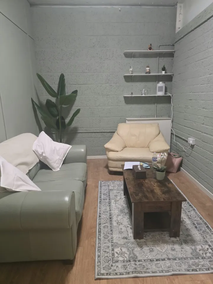 My counselling room: a sage-green sofa and a cream armchair around a wooden coffee table, with plants and shelves